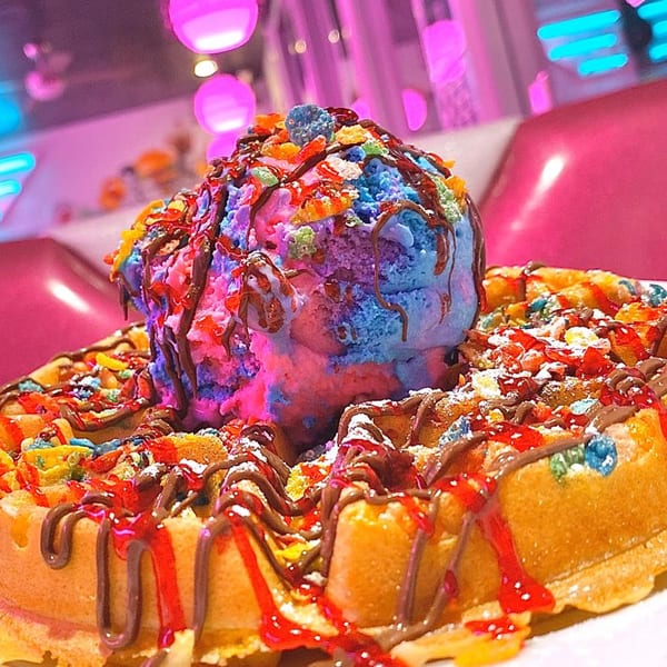 A colorful waffle dessert with blue and pink ice cream, chocolate, and fruit cereal at Beeps Diner.