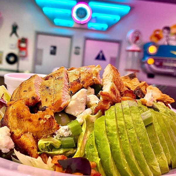 Chicken and avocado salad with feta cheese and olives, in a retro diner setting.