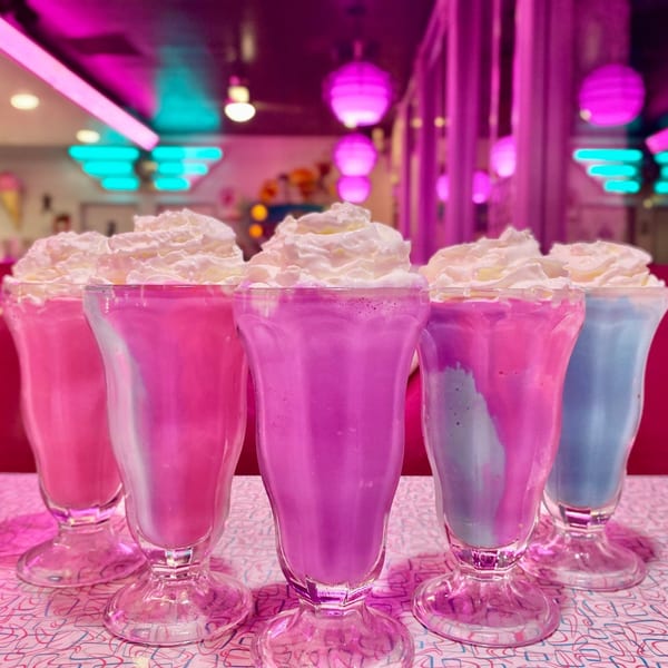 Five vibrant milkshakes with whipped cream, in pink, purple, and blue, at Beeps Diner.