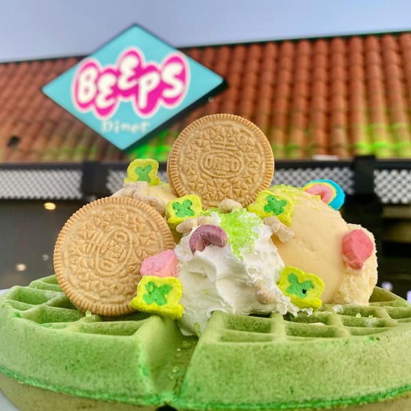A green waffle topped with ice cream, whipped cream, colorful marshmallows, and vanilla Oreo cookies.