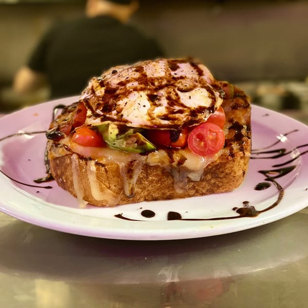 Beeps Diner's thick toast topped with melted cheese, tomatoes, avocado, and a fried egg drizzled with sauce.